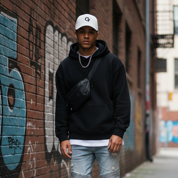 Person wearing a black hoodie and white cap standing against a graffiti-covered wall. main photo 